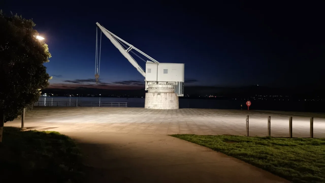 Silueta iluminada de la Grúa de Piedra, con la pluma inclinada y el gancho sobre el paseo