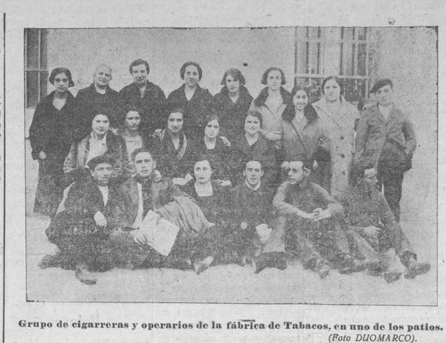 Fotografía y pie impreso de un grupo de cigarreras y operarios en uno de los patios de la fábrica