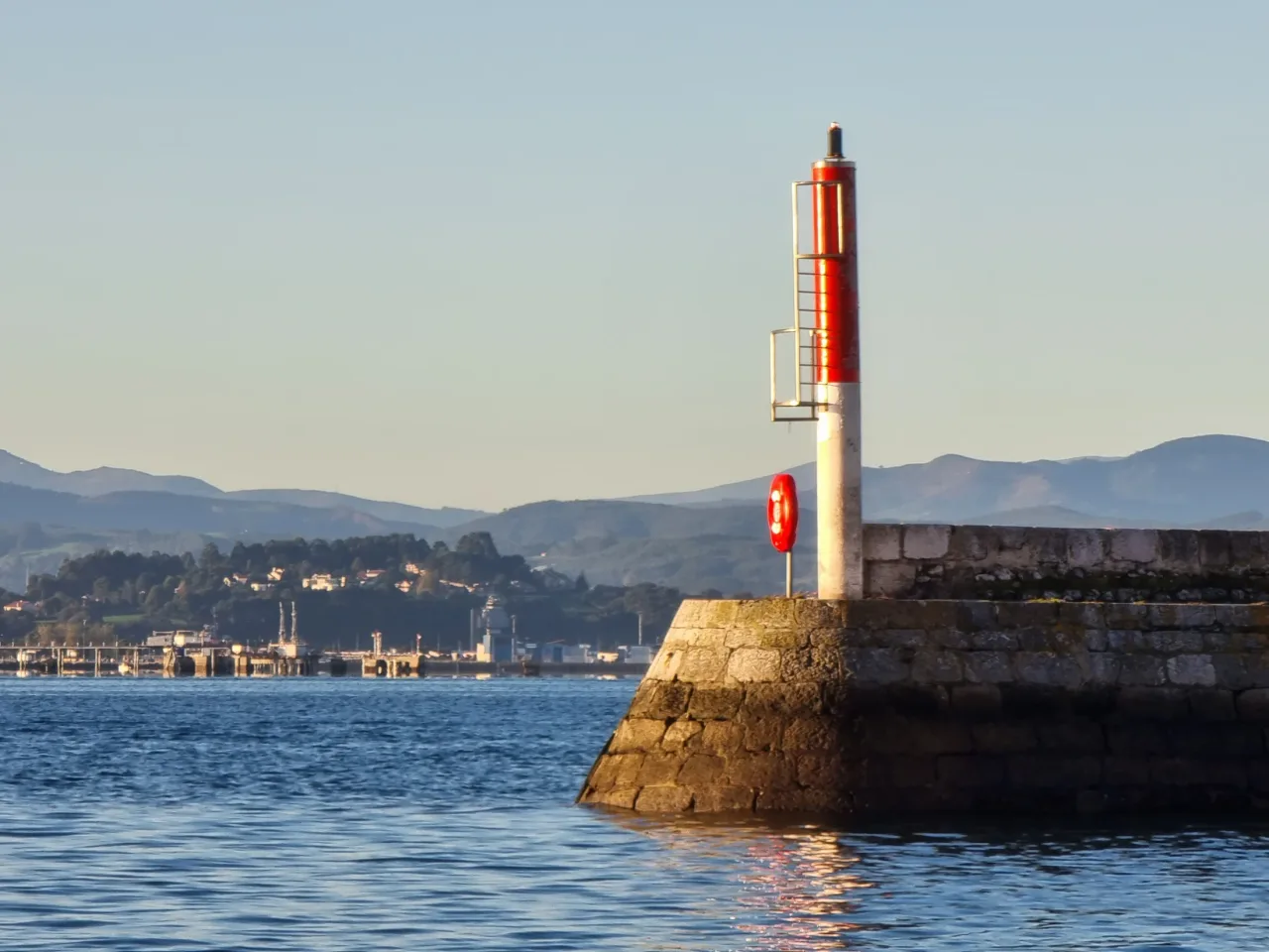 Baliza roja sobre el extremo de un dique de Puertochico, con la bahía detrás