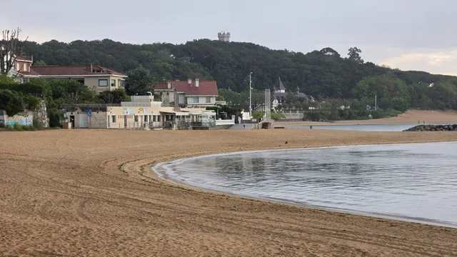 Curva de arena y orilla de la playa de la Magdalena, con el balneario y la península al fondo