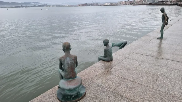 Cuatro figuras de bronce al borde del muelle, dos sentadas, una de pie y otra lanzándose hacia la bahía